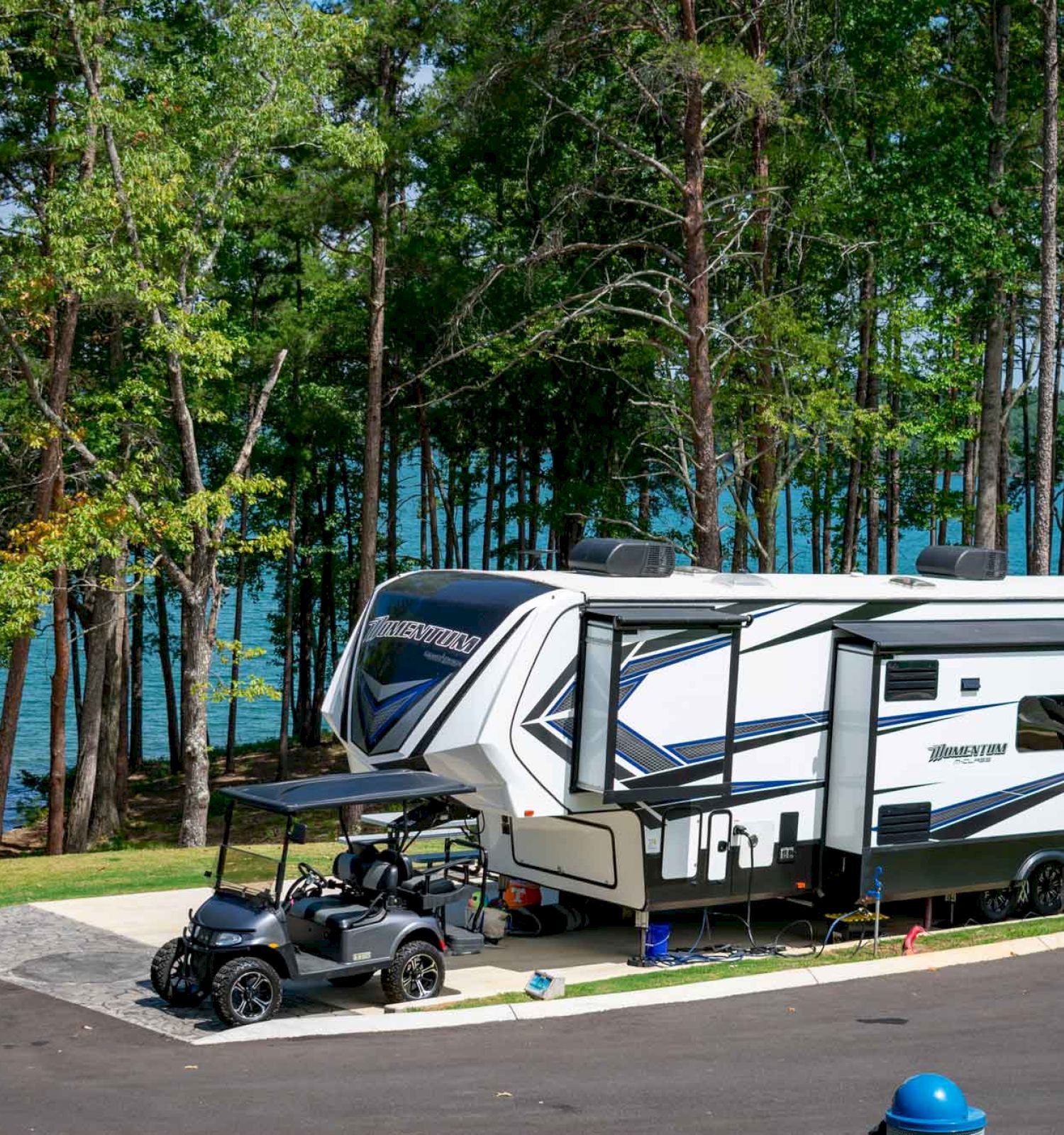 A parked RV with a golf cart by a lake surrounded by trees.
